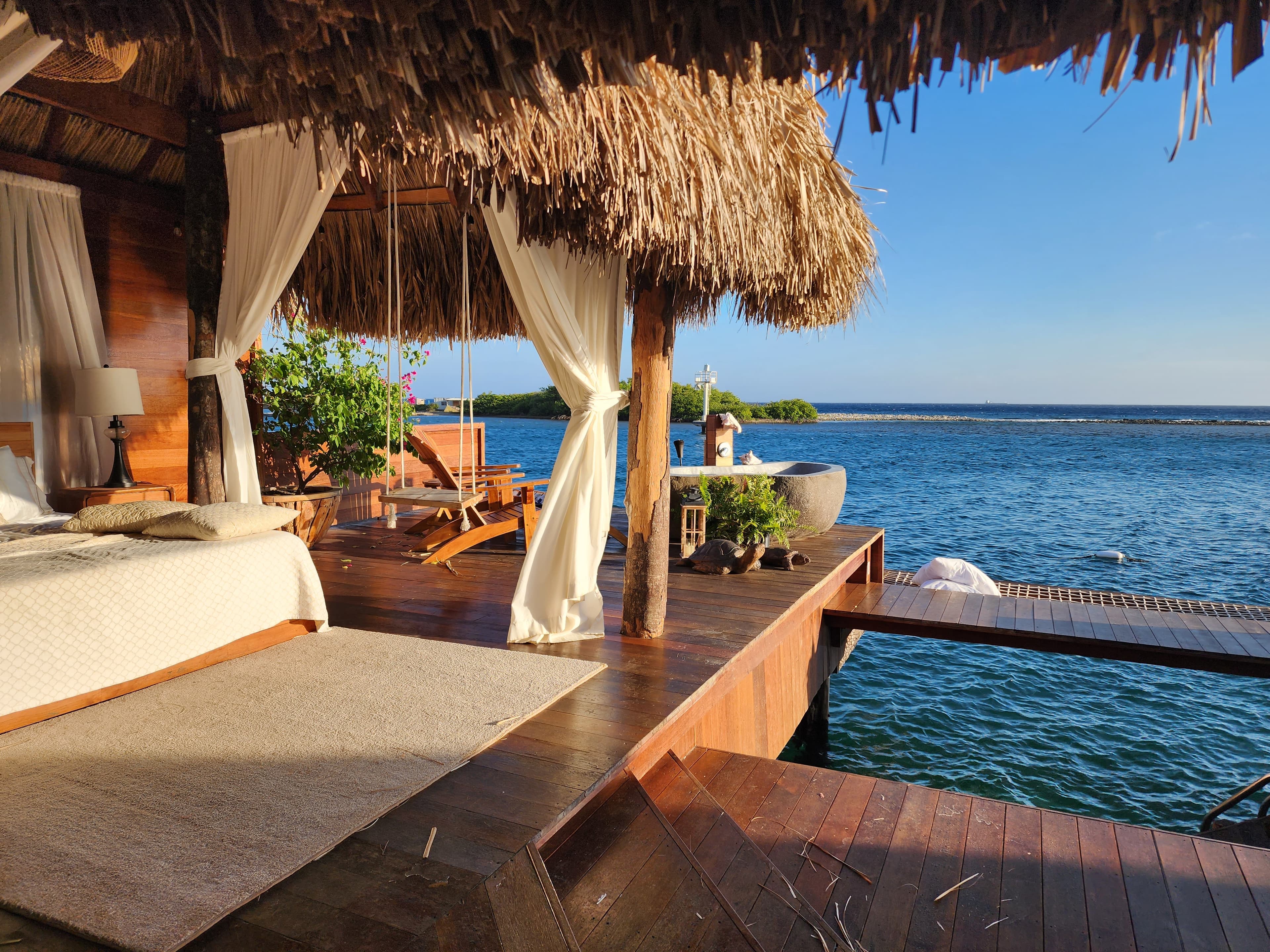 View of a beautiful open-air room with bed and hanging swing, right beside the sea