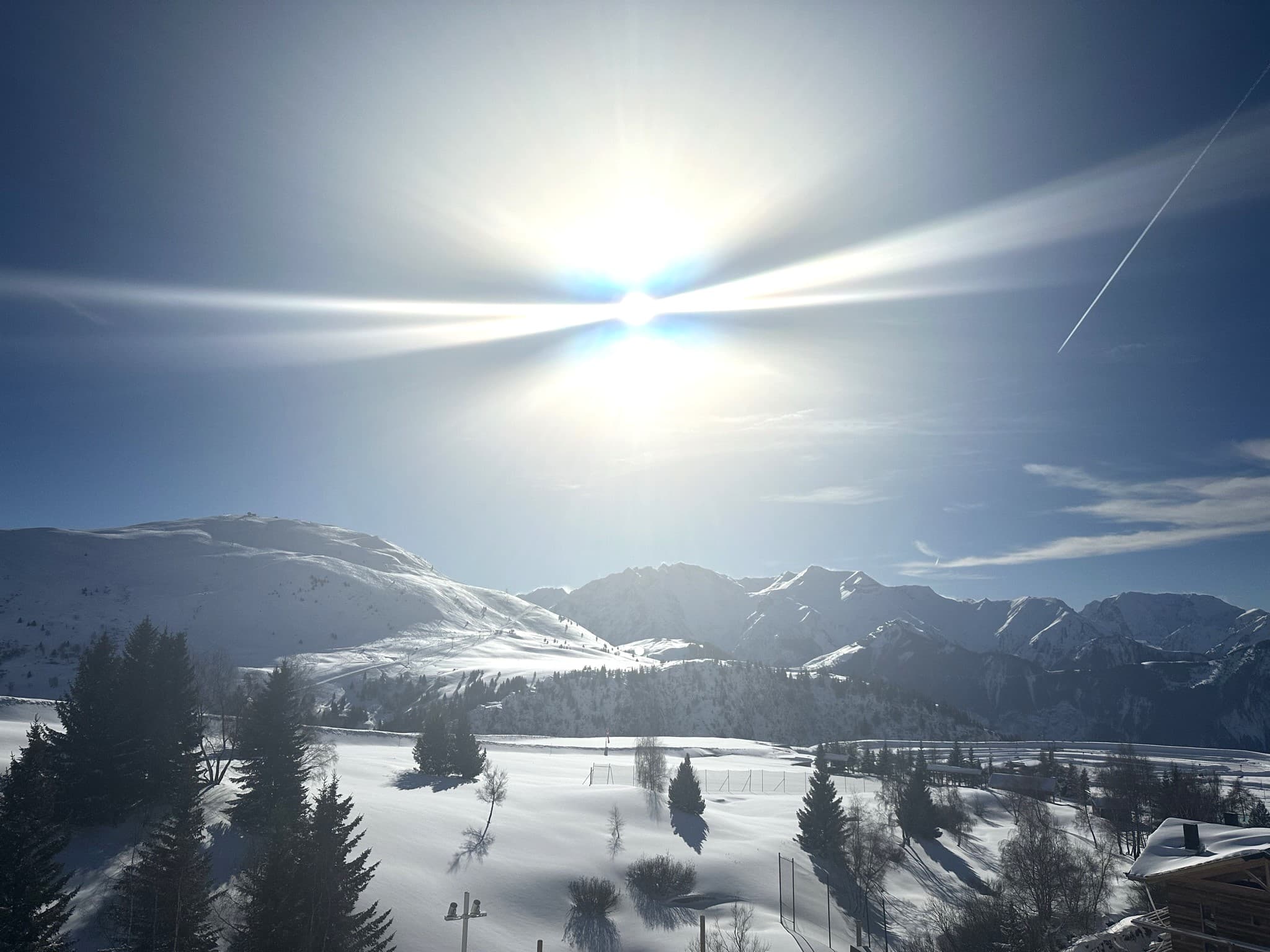 View of the sun shining over snowy mountains dotted with trees