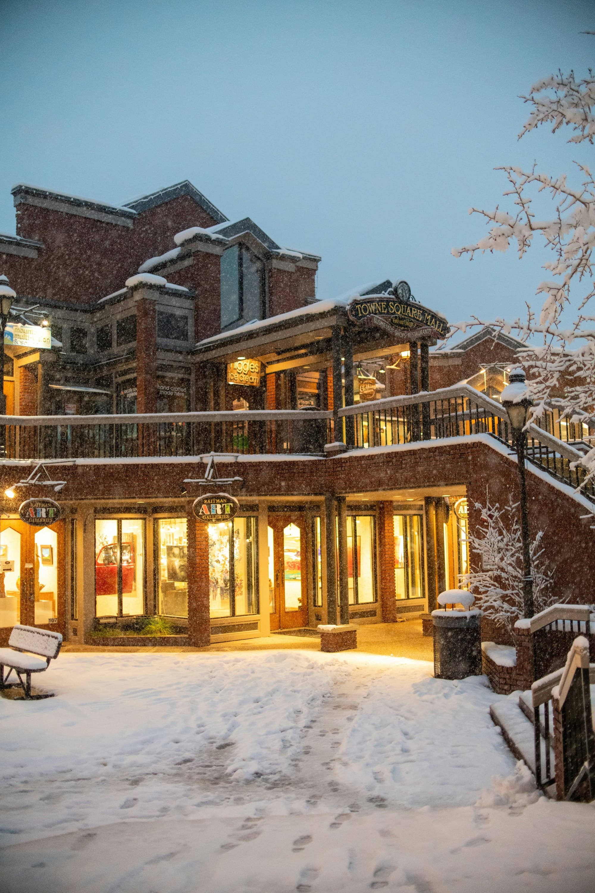 A ski resort with the lights on at dusk surrounded by snow and trees.