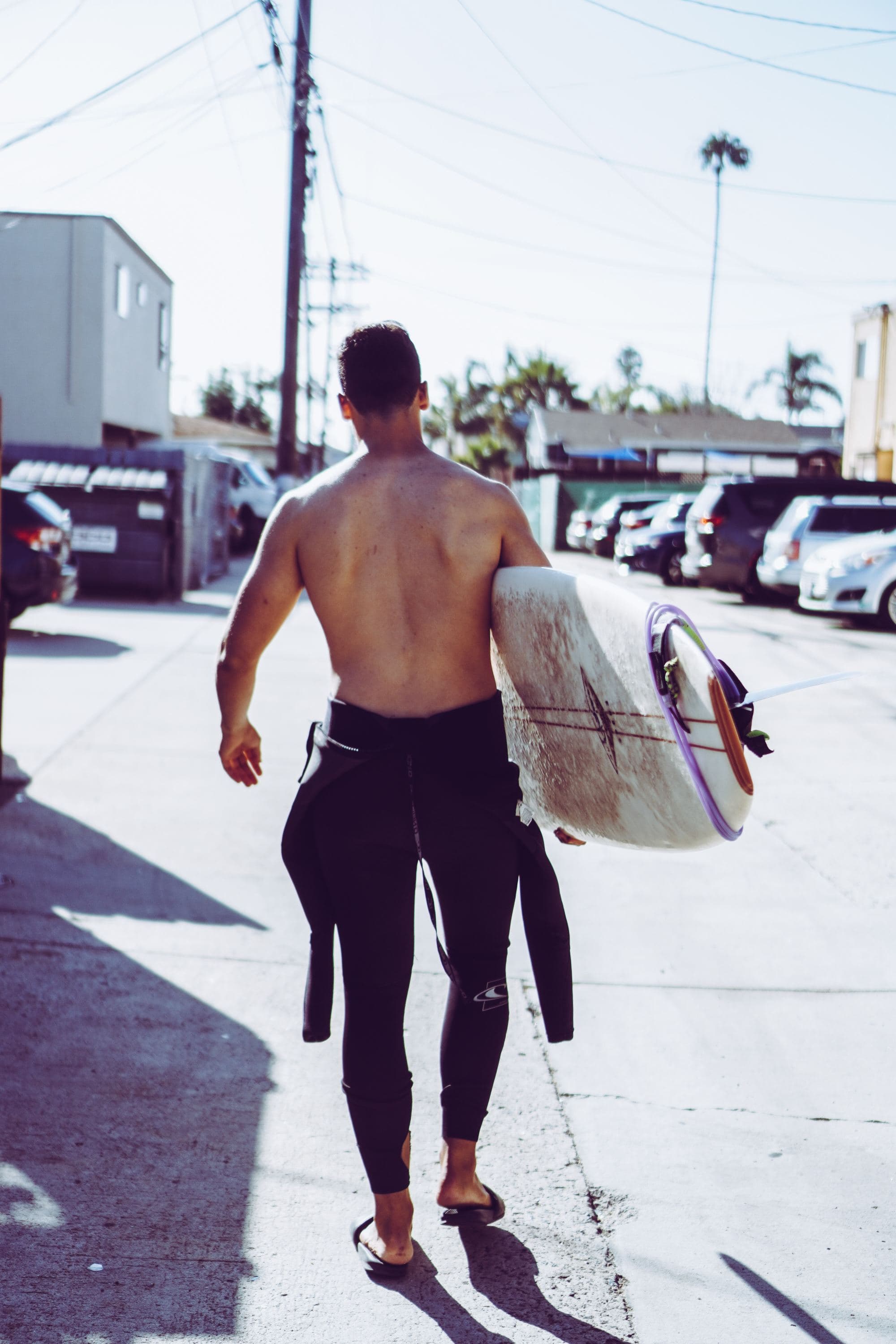 surfer walks with his surfboard down street