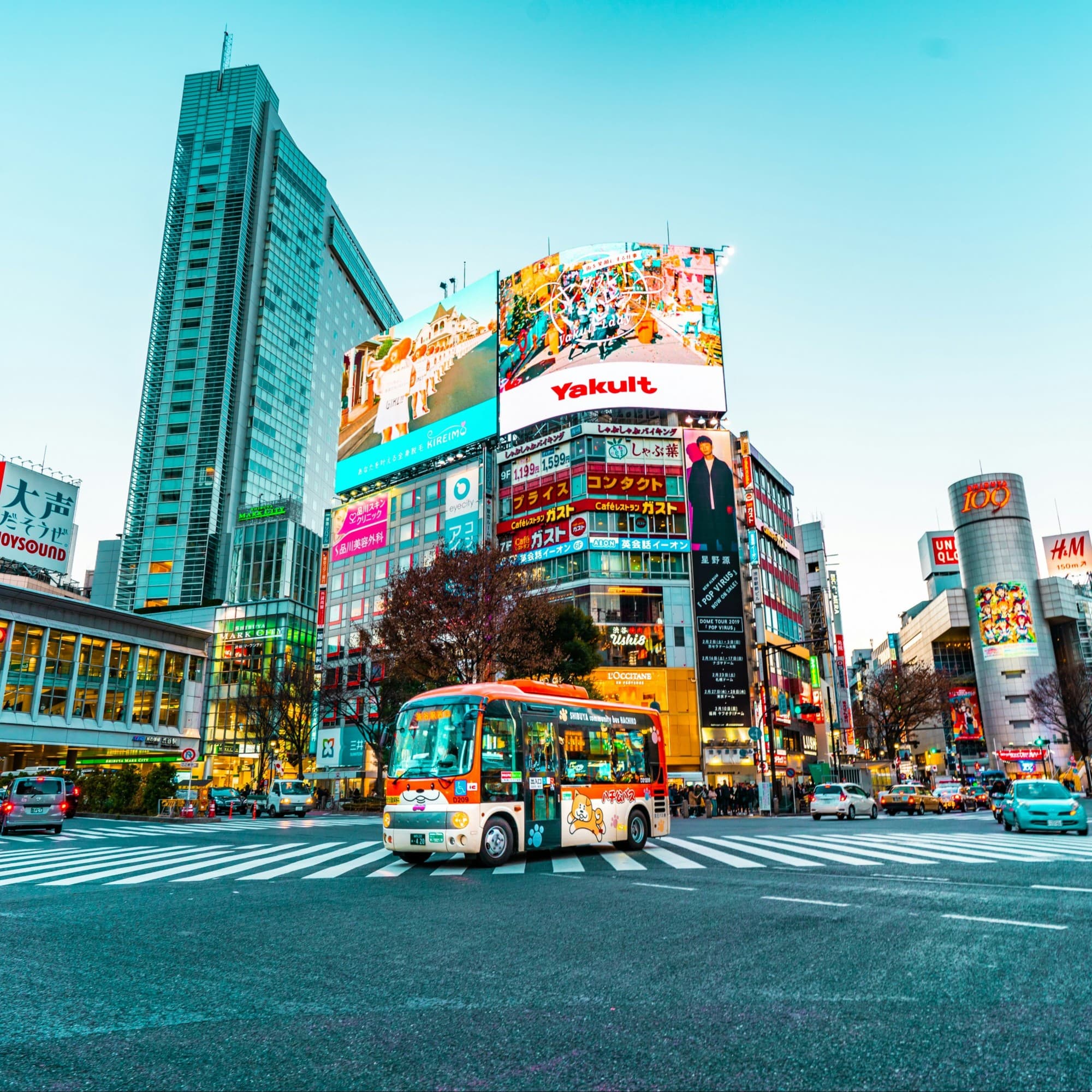 White and red bus on the middle of crossing street during daytime with colorful billboards in the background.