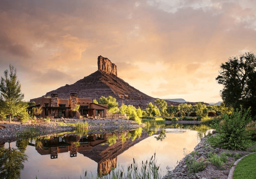 The exterior of Gateway Canyons hotel, with low buildings next to a river in front of a red mountain.