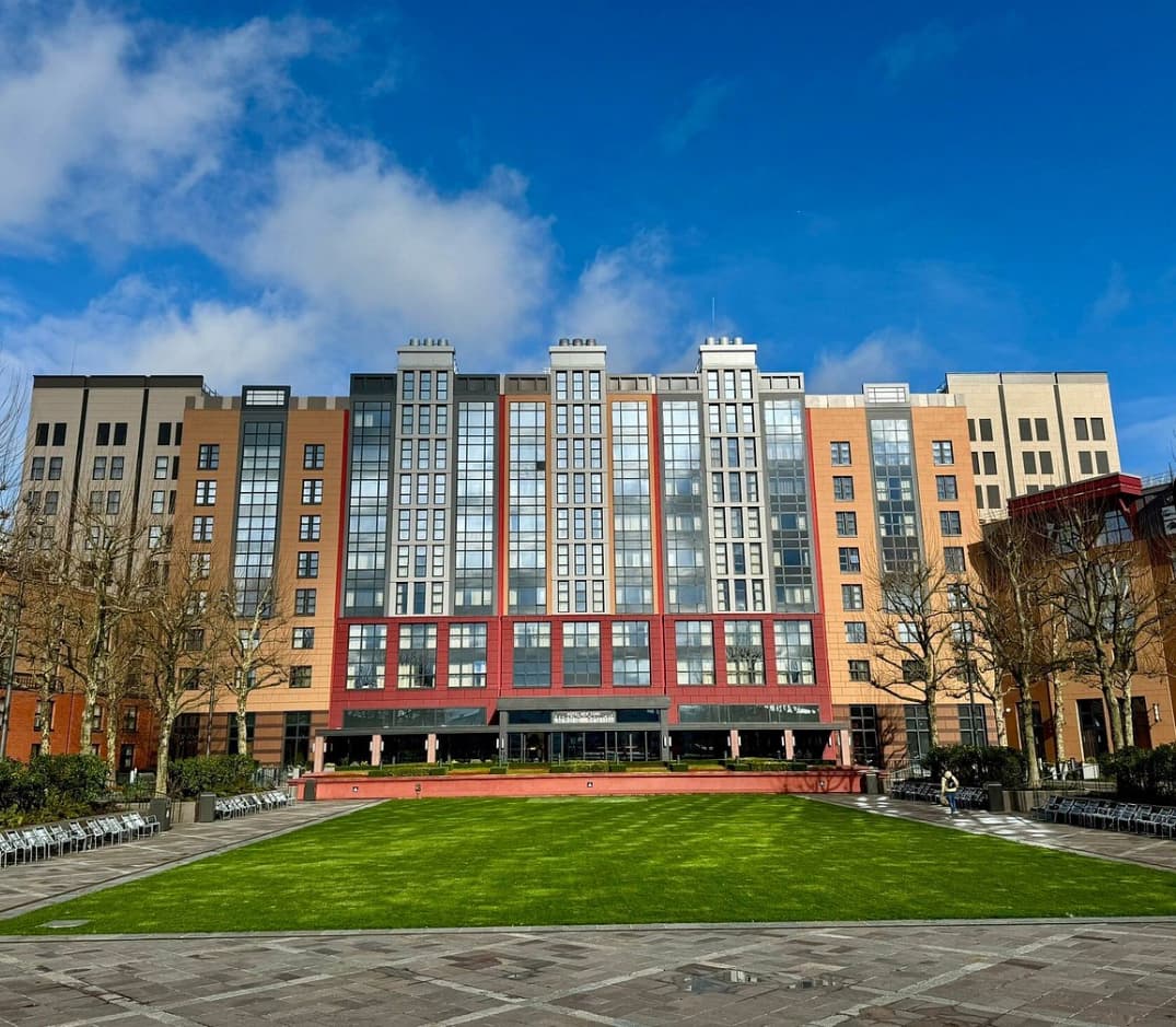The exterior of Hotel New York – The Art of Marvel, the best hotel near Disney Paris, with tall red and orange towers behind a green lawn.