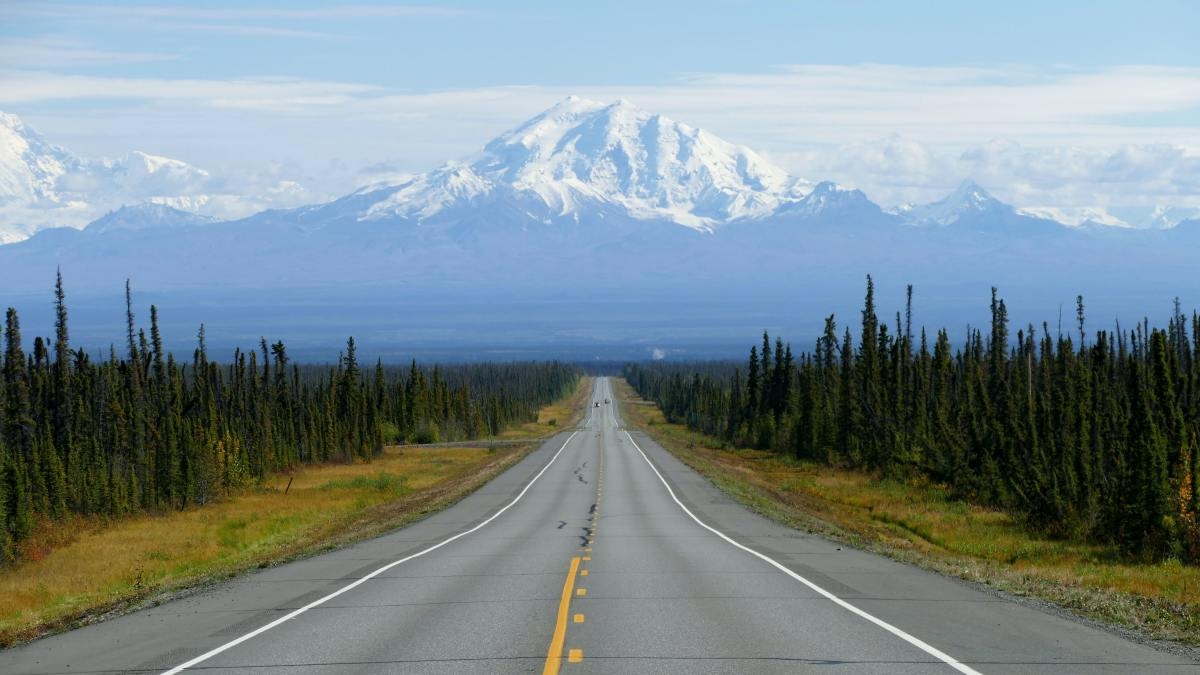 Wide road stretching to snowy mountains in Alaska. 