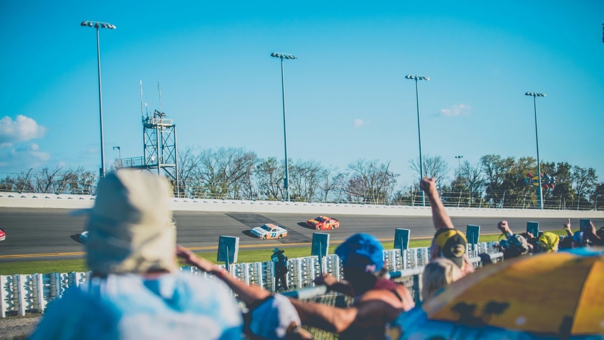 Spectators watch race cars on a banked race track.