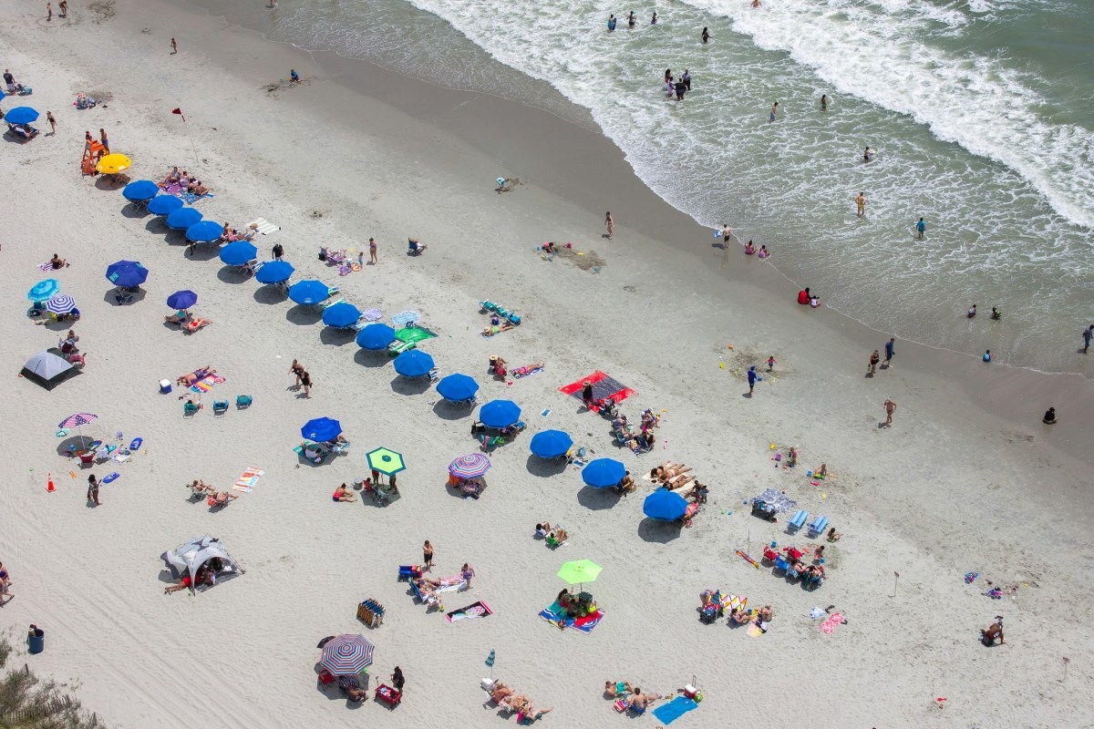 An aerial photo of a beach full of people sunbathing and swimming at the shore. 