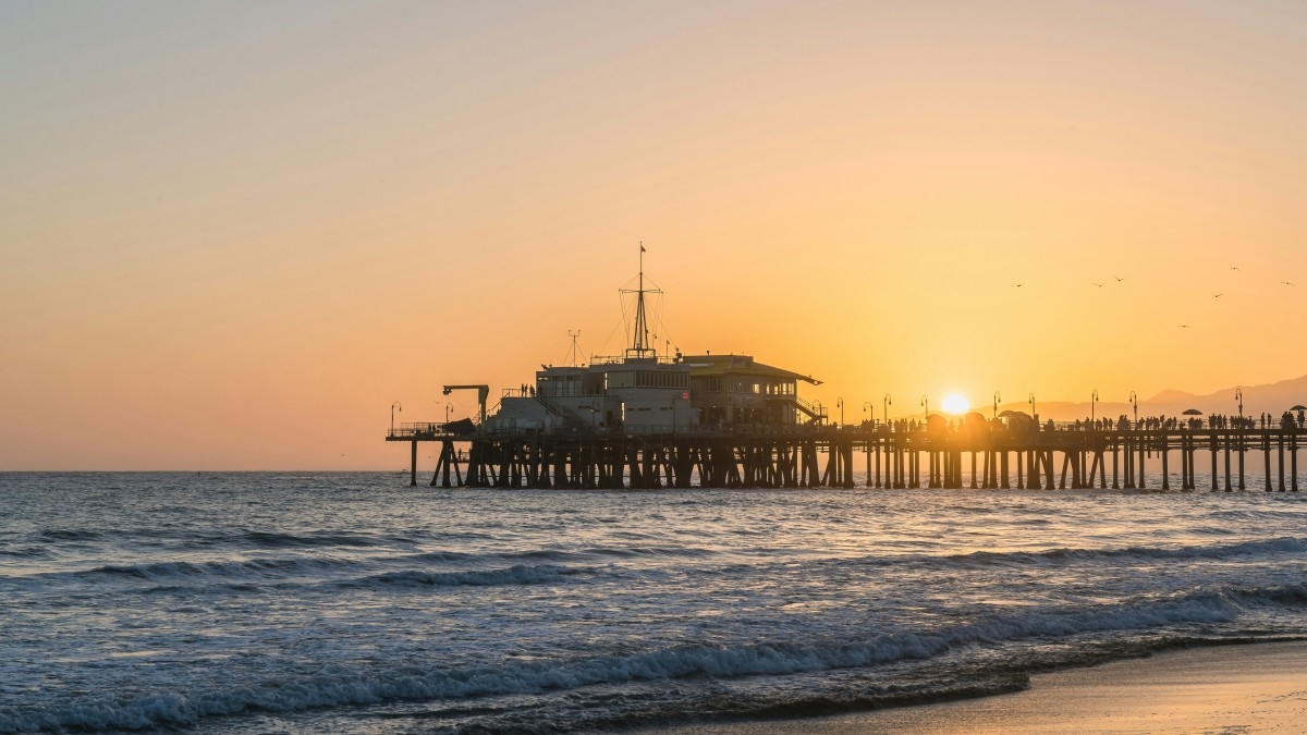 A pier on the ocean with the sun setting behind it.