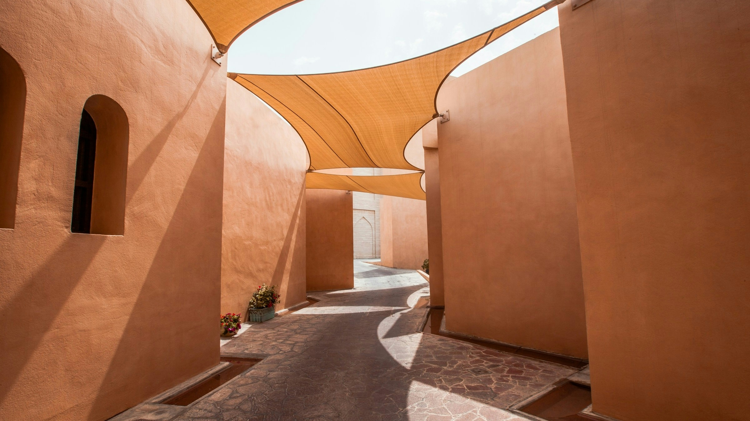 An alleyway in Qatar with clay walls and shade coverings overhead.