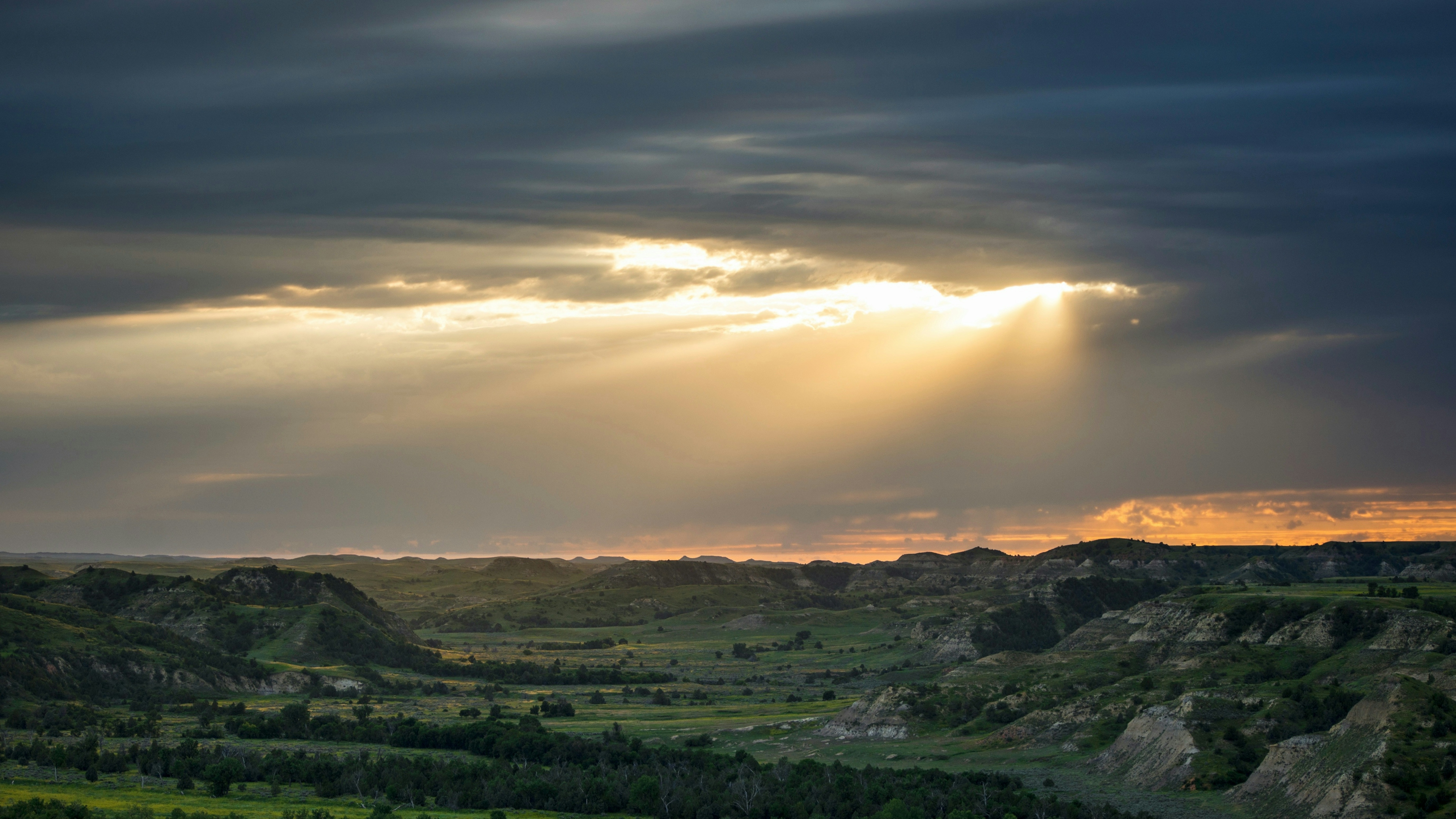 A vast green prairie under clouds with sun peeking through.