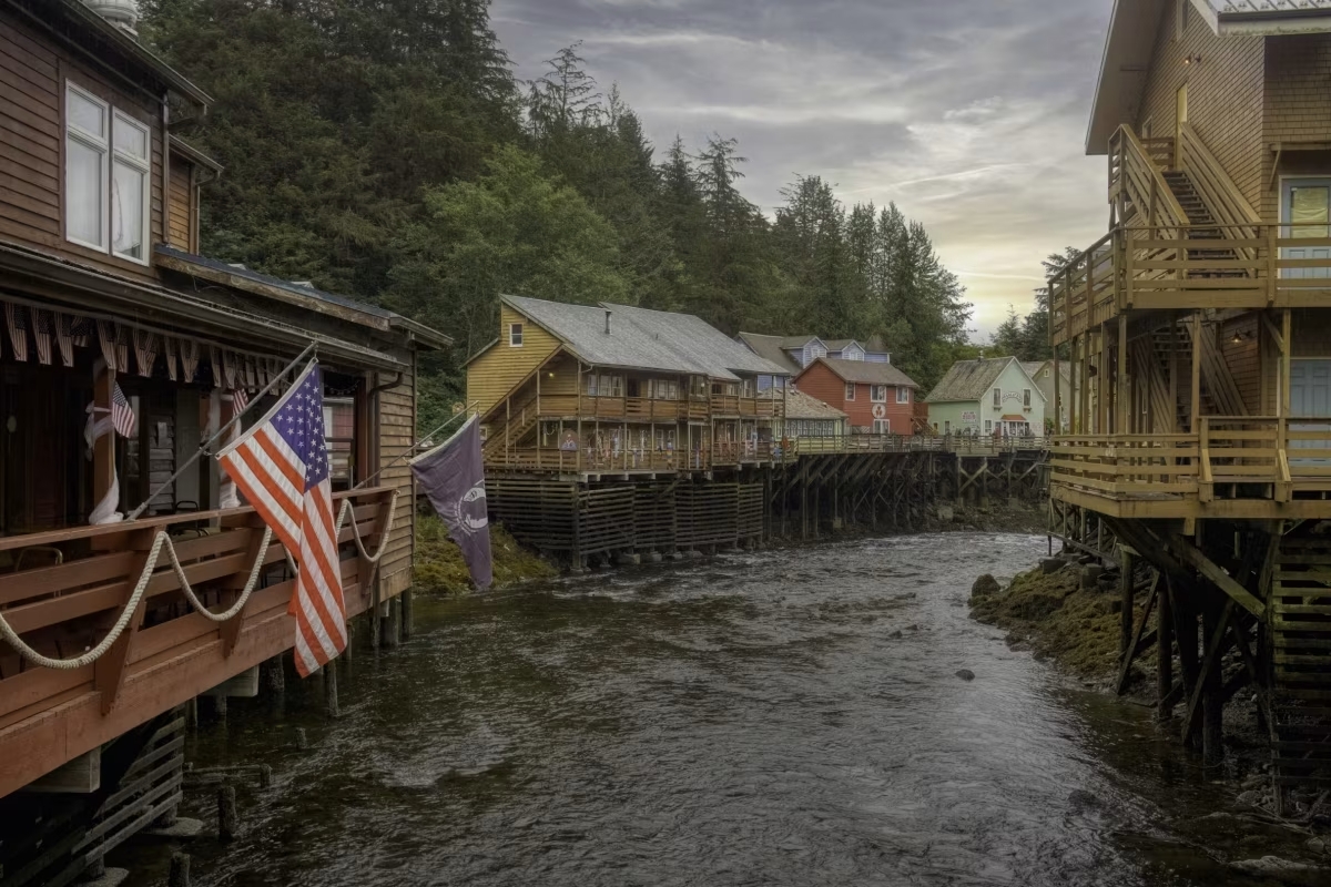 Wooden houses of varying colors built on stilts, lining both sides of a running river. 