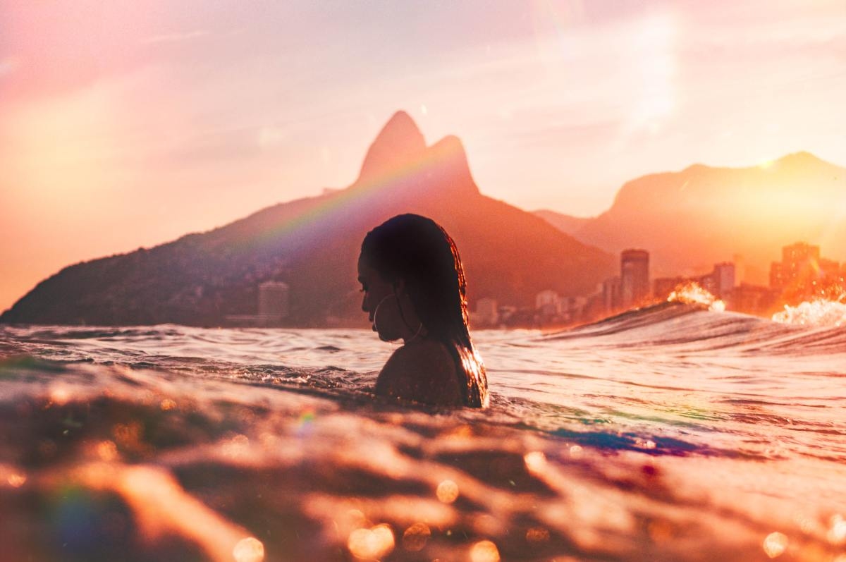 Woman standing in the ocean with her head above water with a city and mountain in the background.