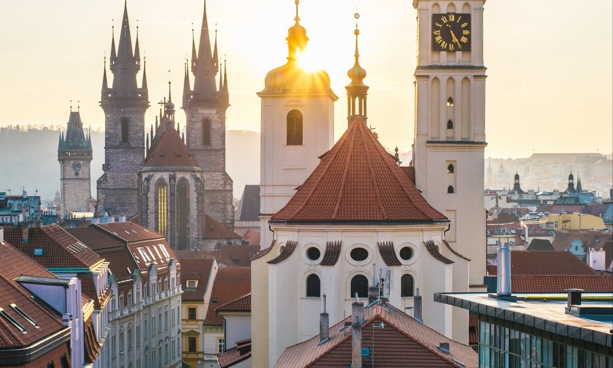 Sunset over historic buildings with brown and turquoise rooftops in Prague.