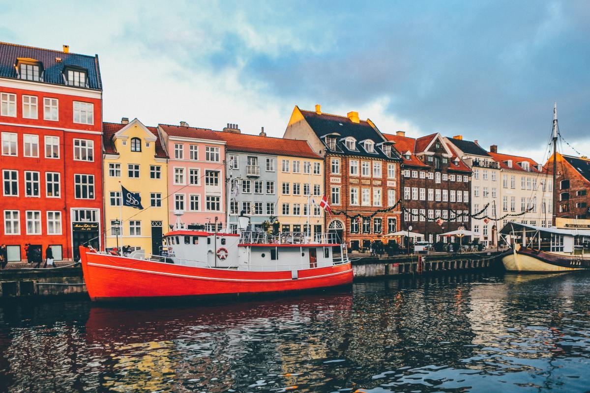 Vivid buildings of Copenhagen along canal with boats parked in front on a bright day.