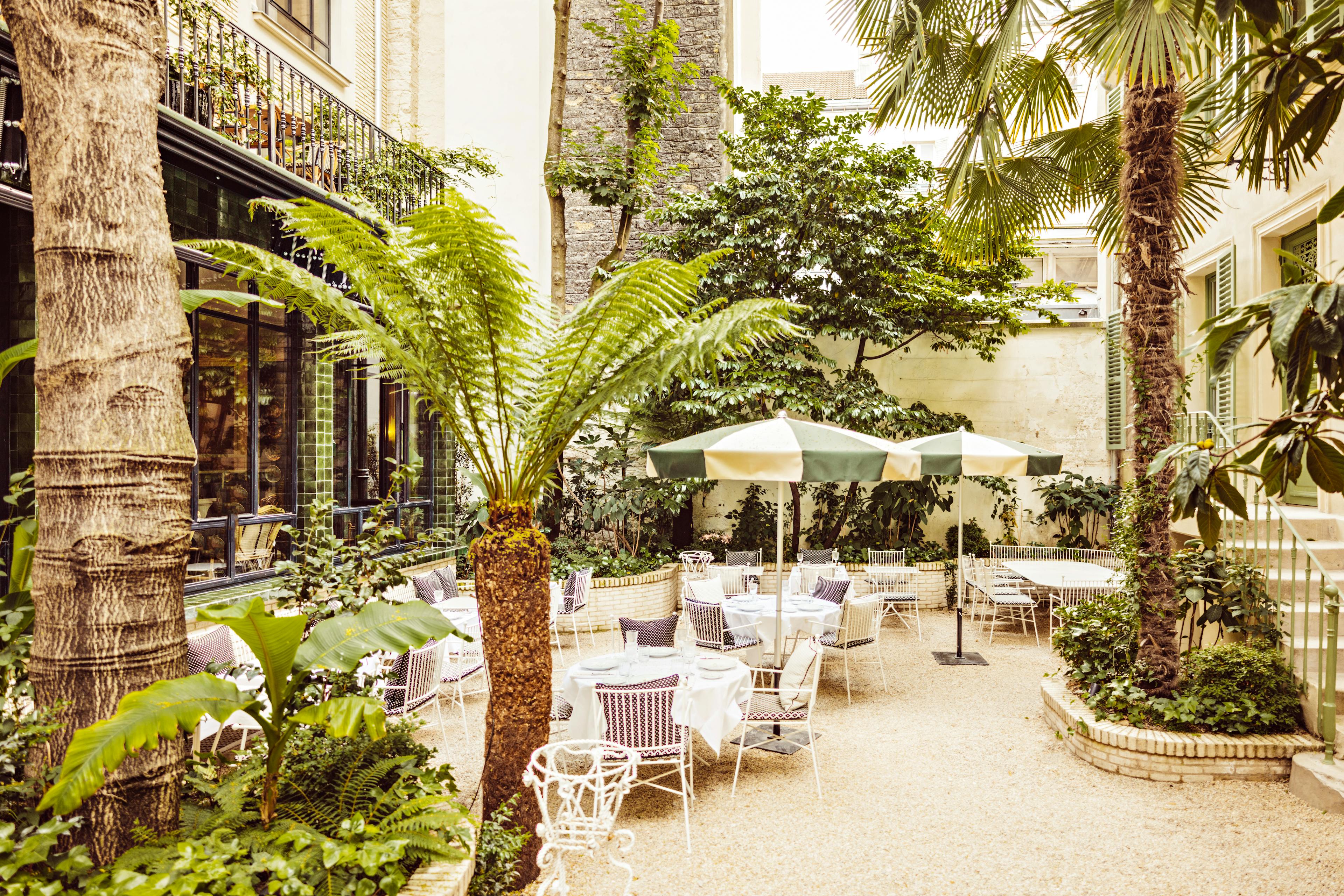 The chic urban garden at the Hotel Eldorado Paris with green and white umbrellas and white tables and chairs surrounded by greenery