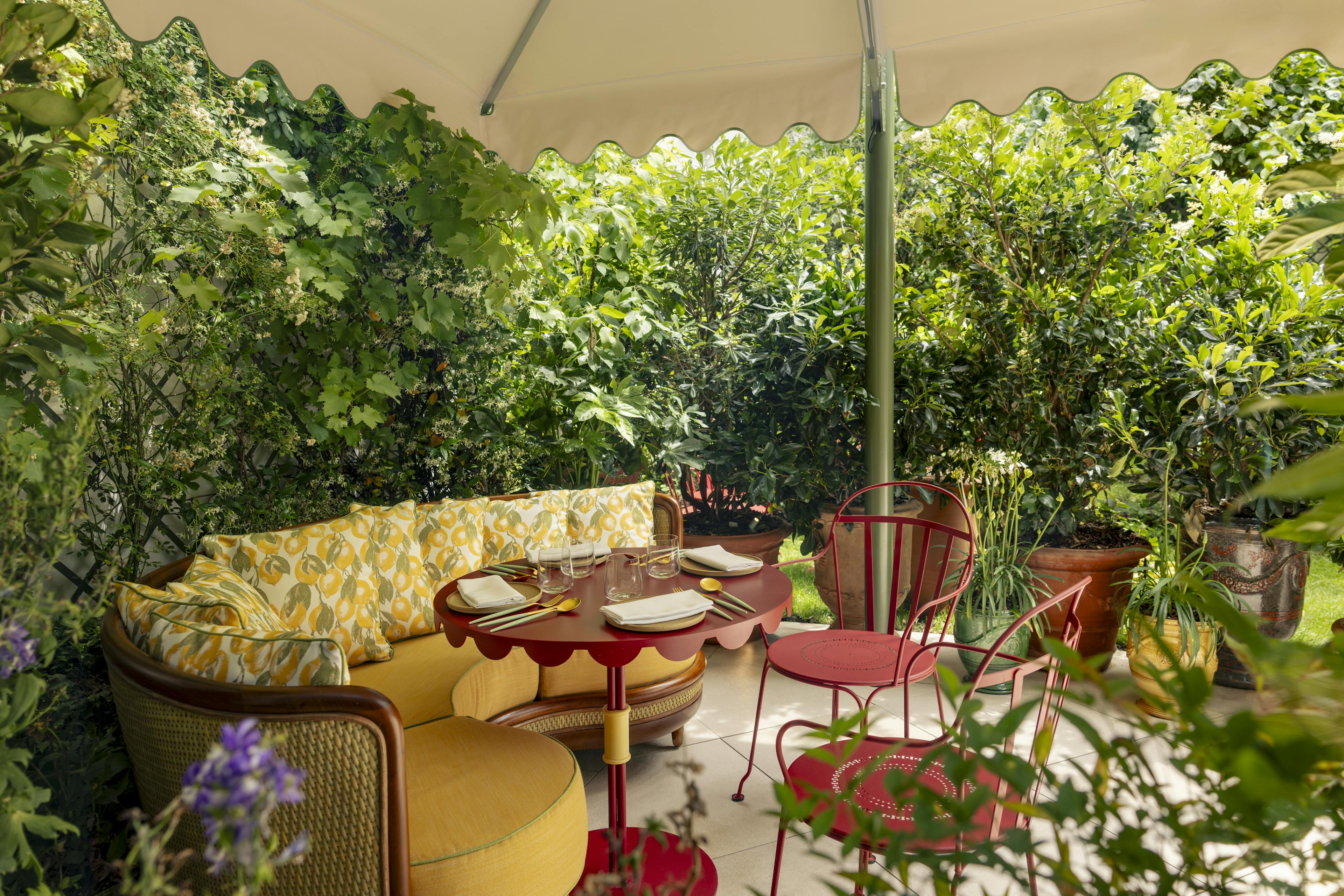 A cozy outdoor dining setup in a garden with yellow sofa and red chairs.