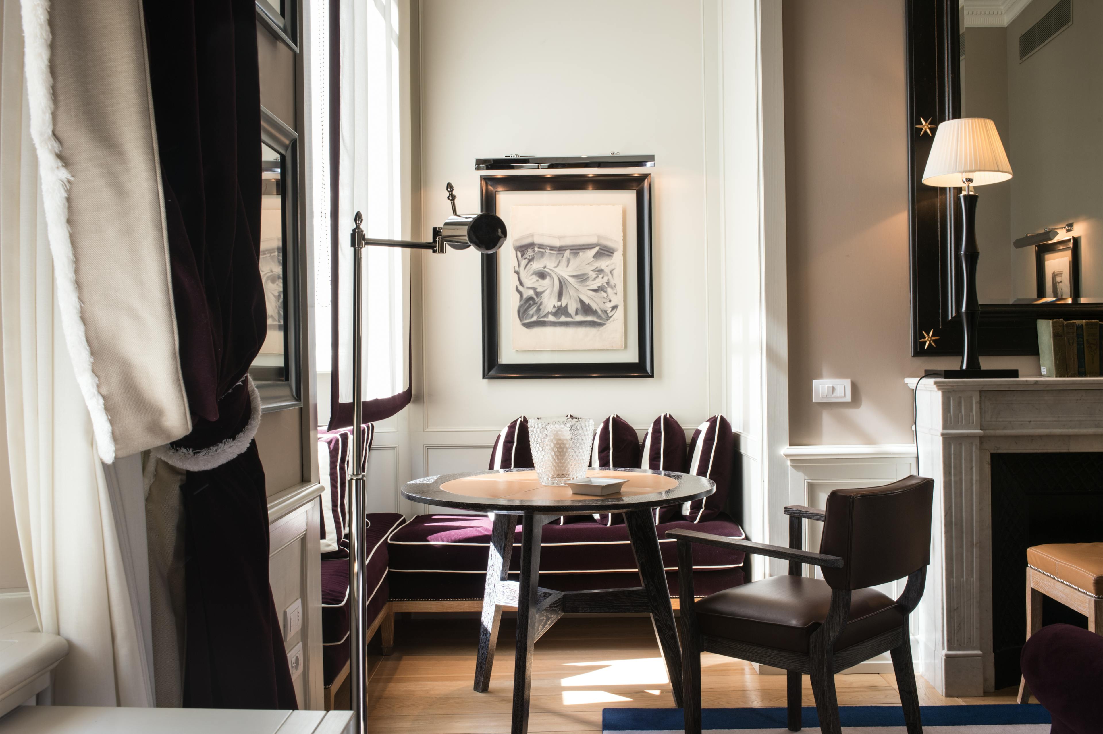 A grand lounge area in a hotel room with purple velvet cushions on a window seat and a fireplace in view