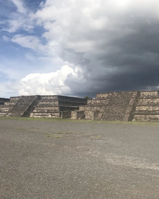 A picture of three pyramids and an open sidewalk under a stormy grey cloud