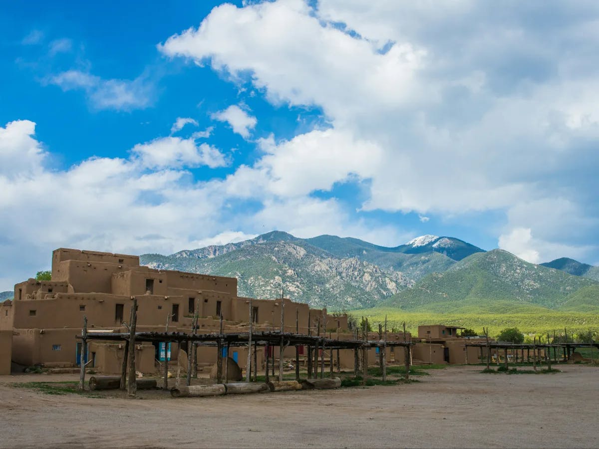 A picturesque adobe structure stands against a mountain backdrop under a vast blue sky.