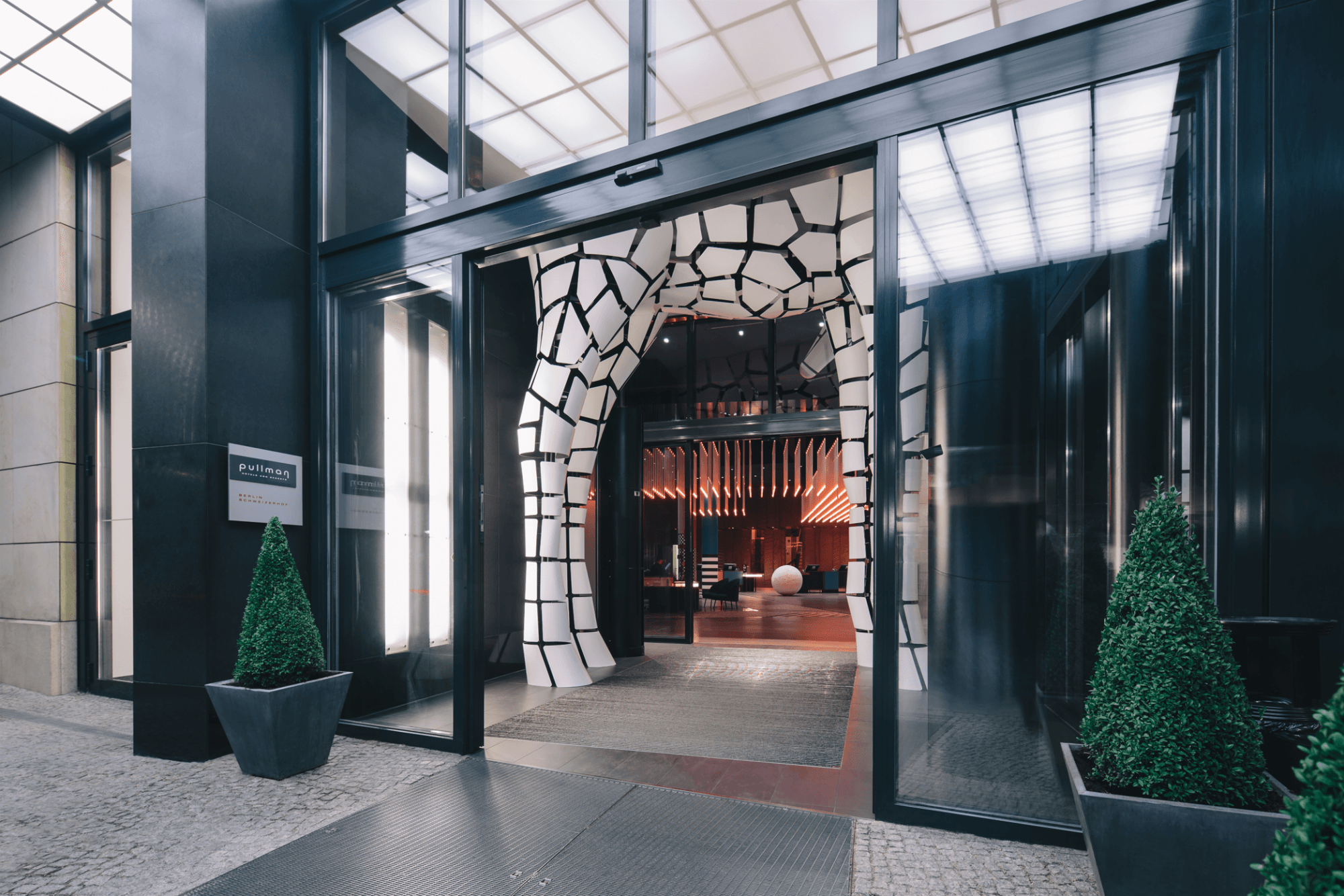 Entrance to the Pullman Berlin Schweizerhof in Berlin, Germany with glass door and a white tile entryway. 