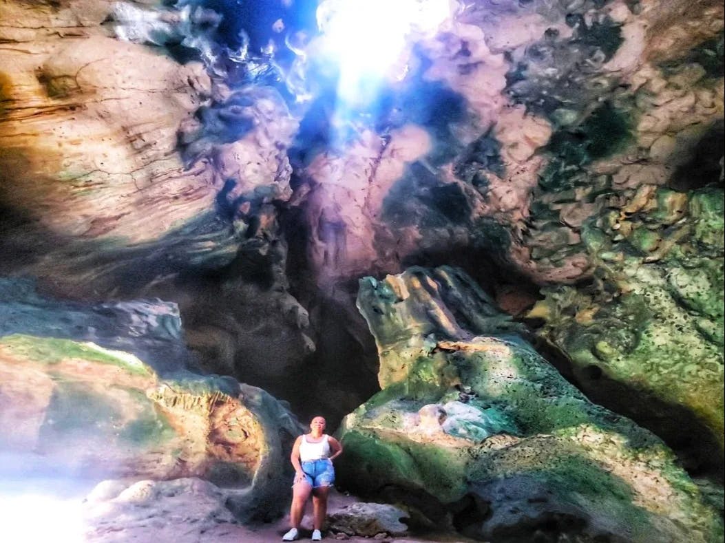 A person in a cavern with sunlight highlighting the rocky textures and creating a dramatic atmosphere.