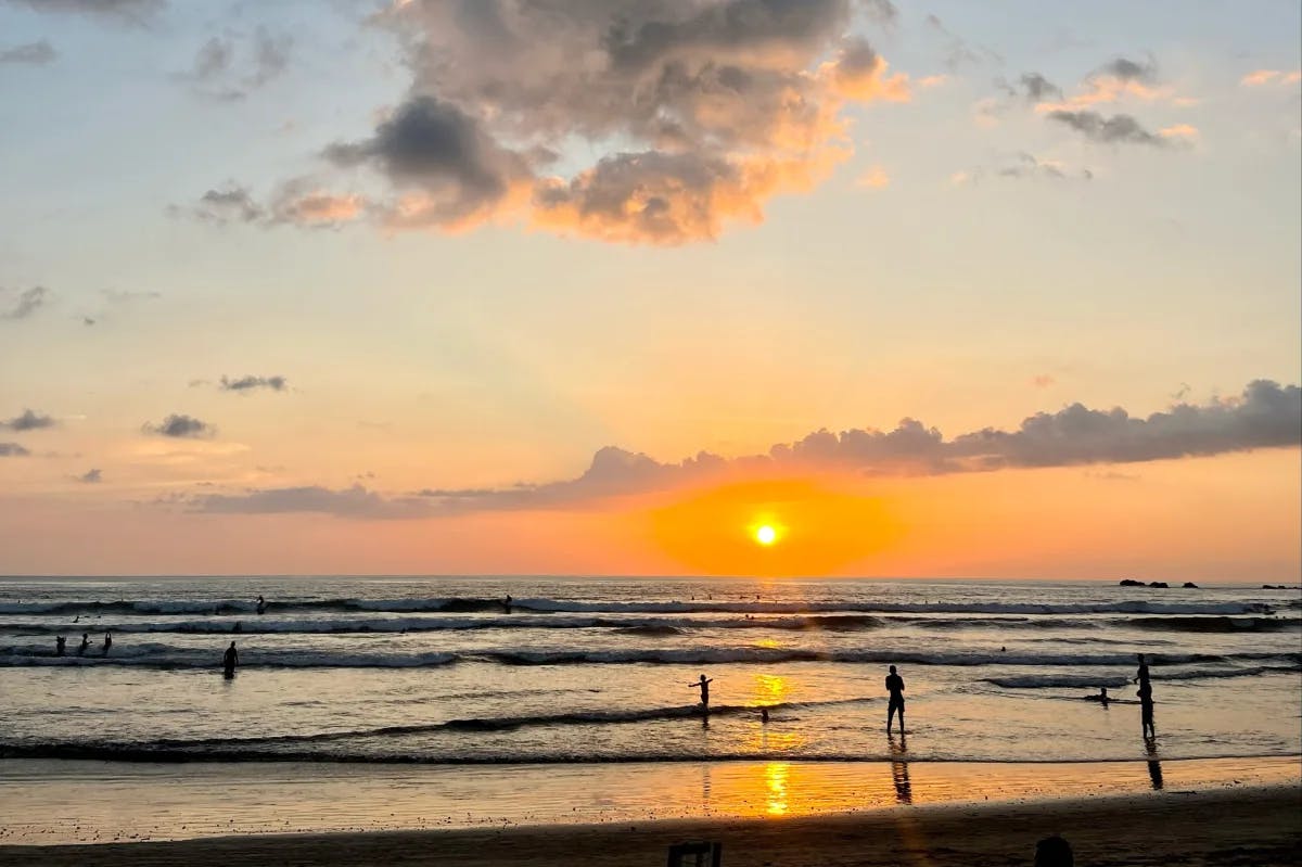 Sunset at Playa Guiones with silhouettes of people playing and swimming in the water.