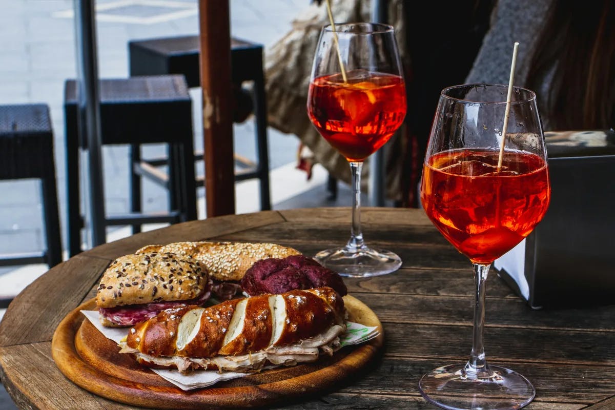 A wooden table with a plate of bread and two Aperol spritzes.