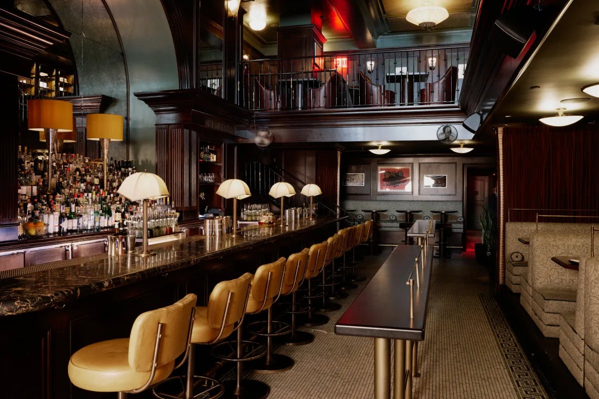 A view of a bar at the Ned NoMad hotel in NYC with wood paneling, booths, and leather bar chairs