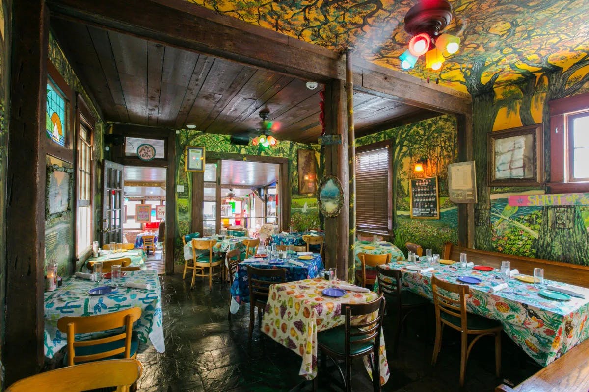 The interior of Jacques-Imo's Cafe, with colorful wall art on all walls and ceiling and multicolored tablecloths.