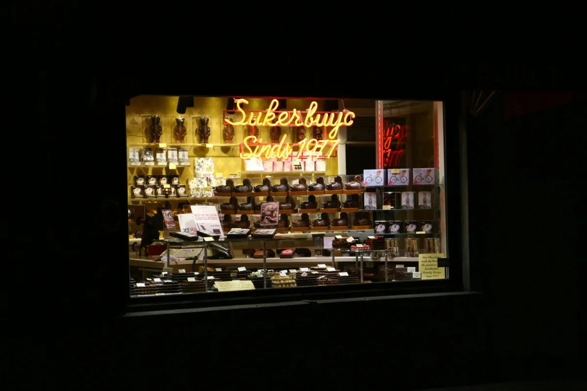 A storefront window with a lit yellow neon sign and merchandise being displayed at night. 