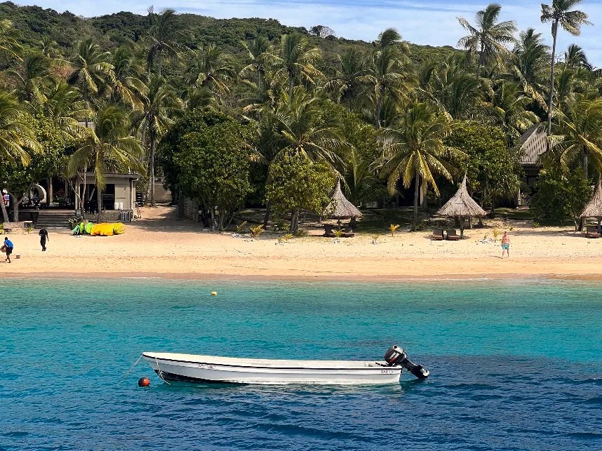 White speed boat on water body with beach in the background.