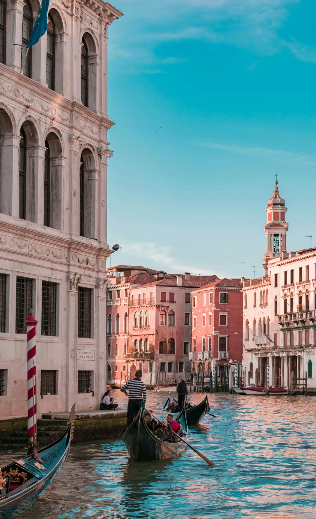 Venetian gondolas and gondoliers transporting tourists through Venice's canals, with classic architecture and buildings to view along the way.