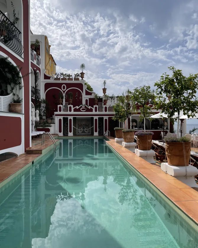 View of a long empty hotel swimming pool next to a red building with white trim on a sunny day