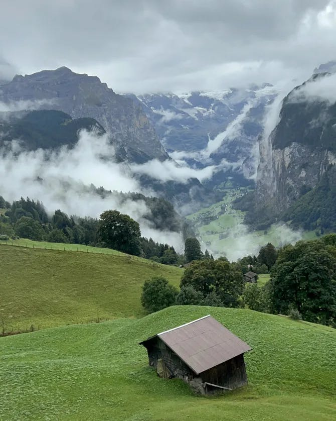 Beautiful view of the mountains with low clouds around and a small brown house on a grassy hill