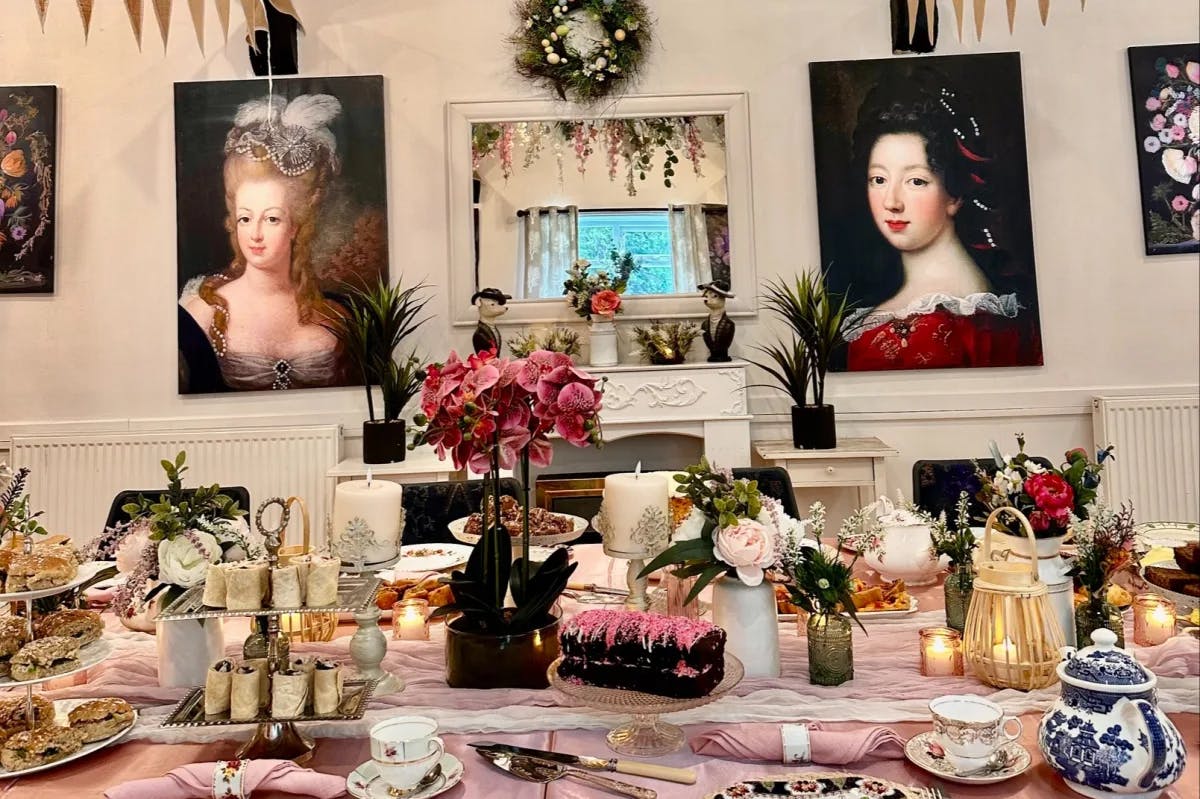 An afternoon tea at The Old Rectory Pop-up Tearoom with rich furnishings, wall hangings and an ornate table setting of finger foods and other delicacies.