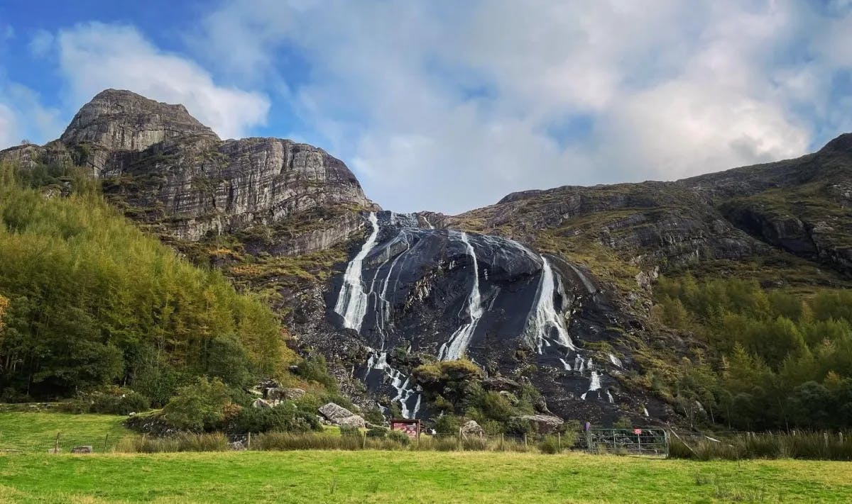 Cascading waterfalls down a cliffside onto a green lawn at Gleninchaquin Park during the day.