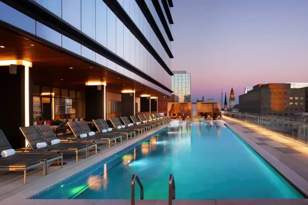 Loungers line one side of a long, rooftop pool lit up at twilight