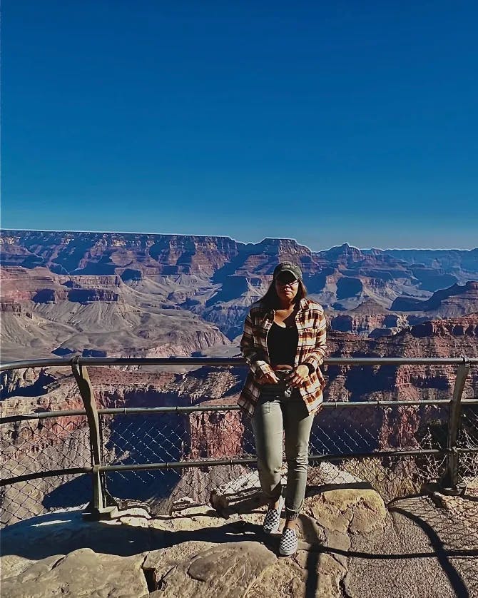 A woman posing against a metal railing in front of a view of the Grand Canyon.