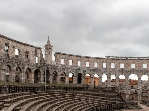 An inside look at the ancient Pula Arena, designed like an amphitheater, with as stone structure and seats, on a cloudy day.