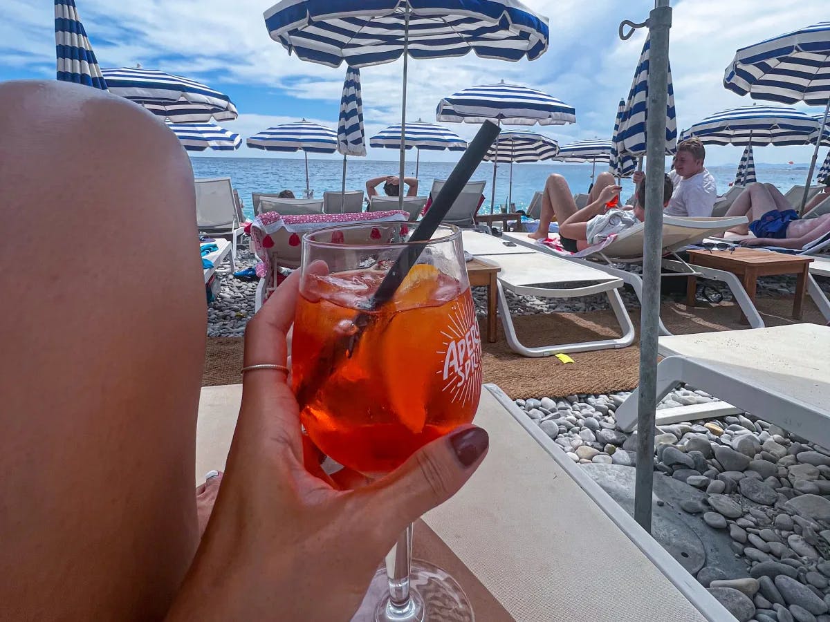 A person holding a glass filled with cocktail near the beach during daytime.