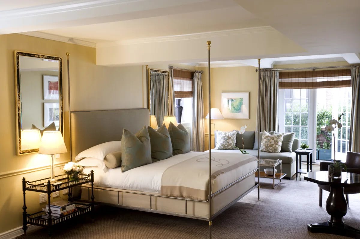 a four-post bed in an elegant hotel room with white doors opening onto a terrace