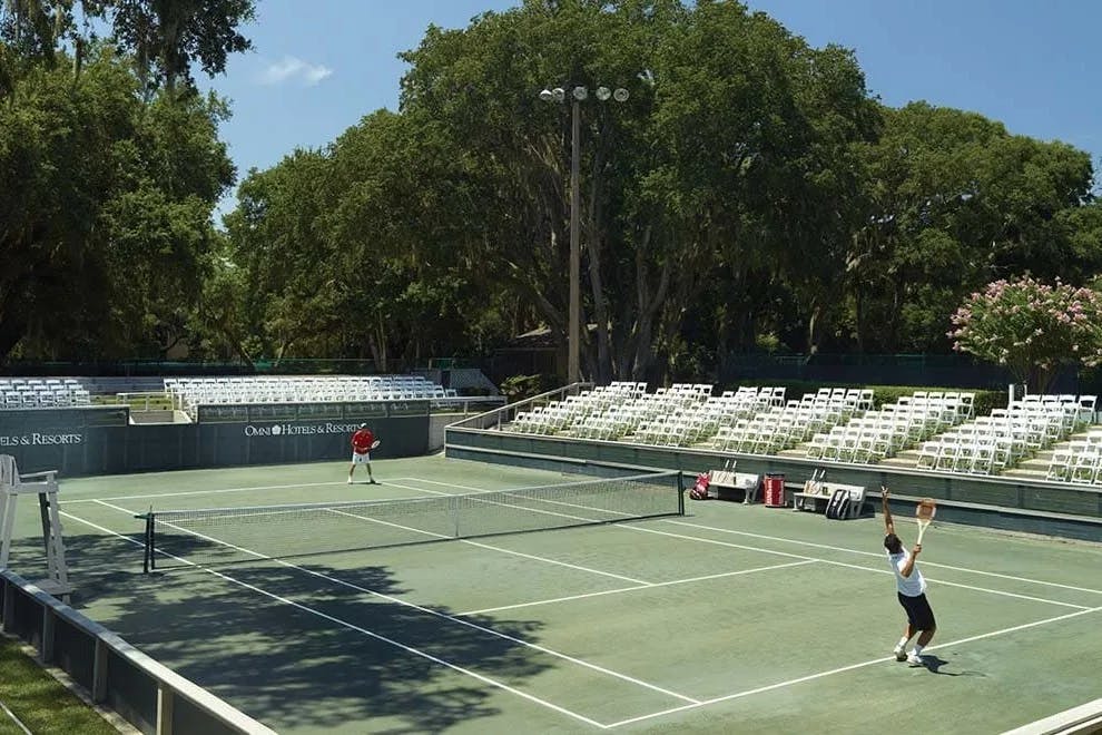 aerial view of a green tennis court surrounded by white chairs and tall trees