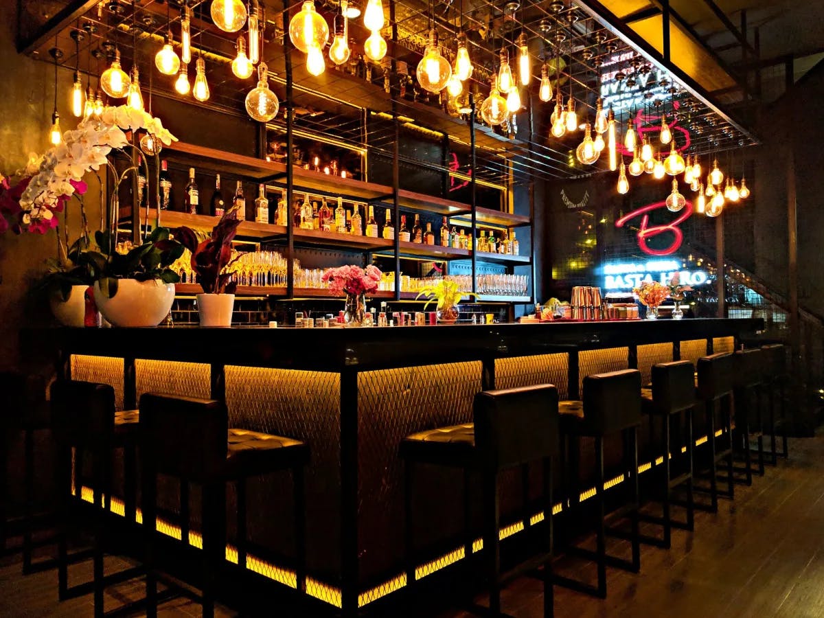 A well lit bar counter with stools and wine bottles. 