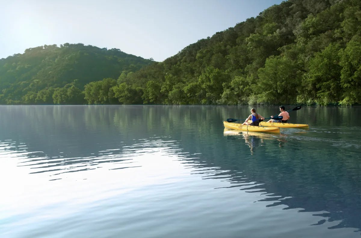 two people paddle yellow kayaks on a hillside lake