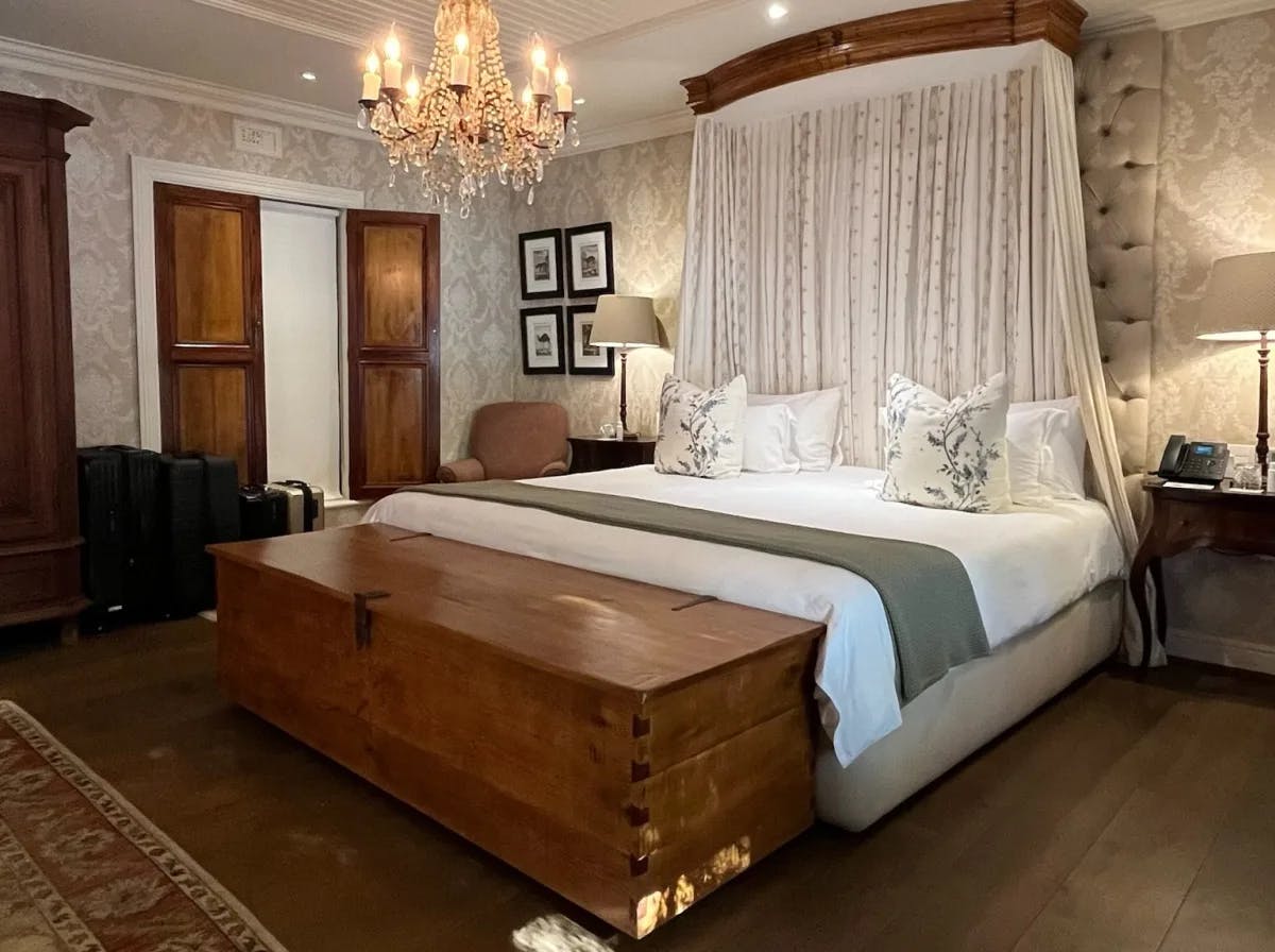 The interior of a hotel room at Lanzerac Wine Estate with wood fixtures and a white drape hanging down from the ceiling over the bed