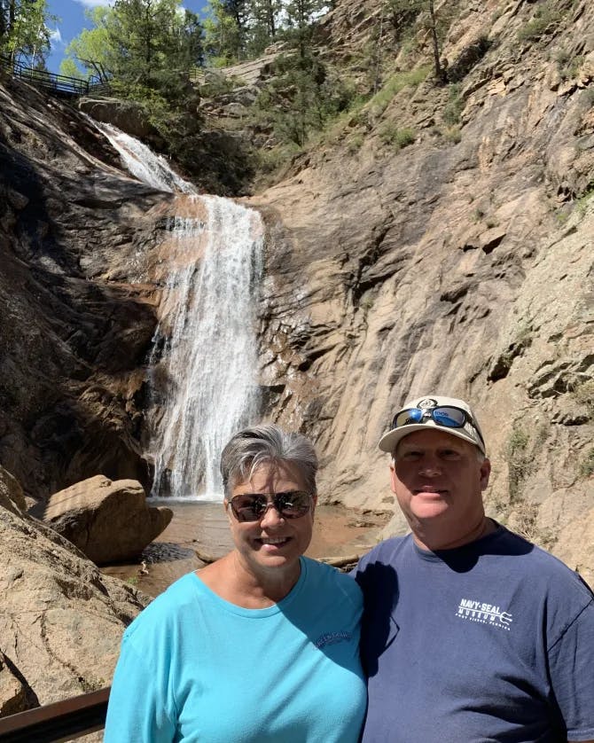 Picture of Robyn and husband standing in front of a waterfall surrounded by rocky terrain