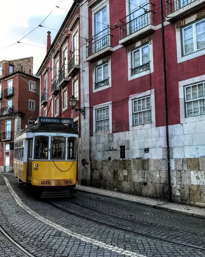 View of a yellow trolley coming down the track besides a red building in Lisbon