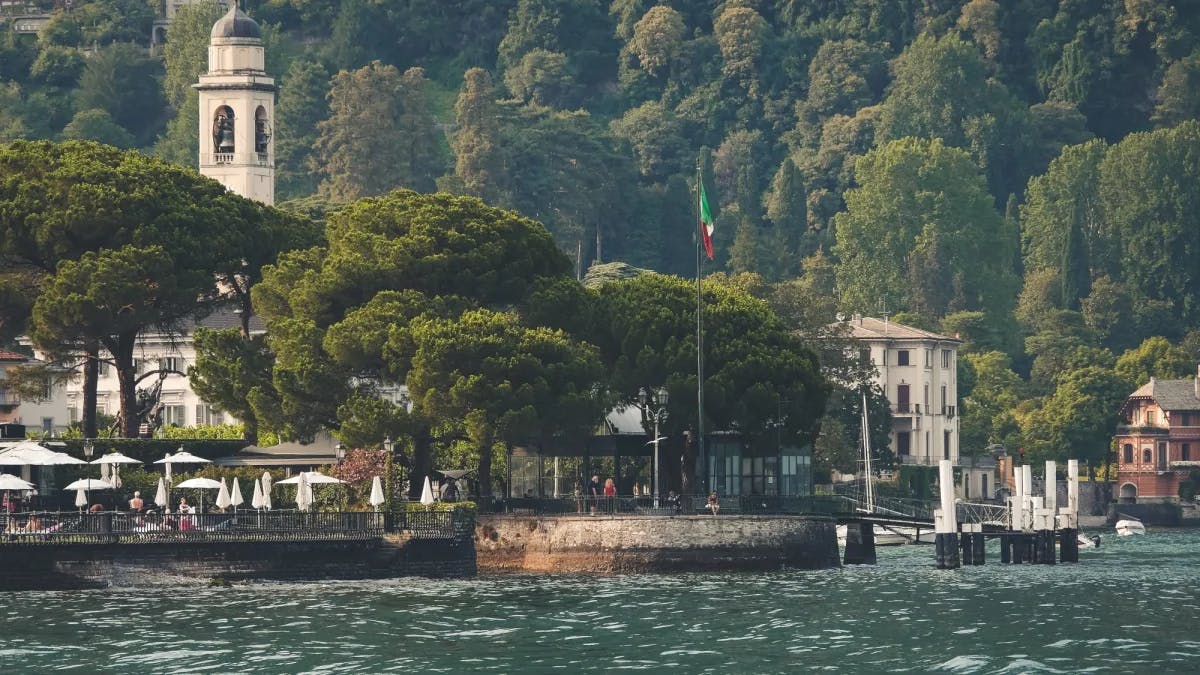 Lake with trees, buildings and outdoor sitting.