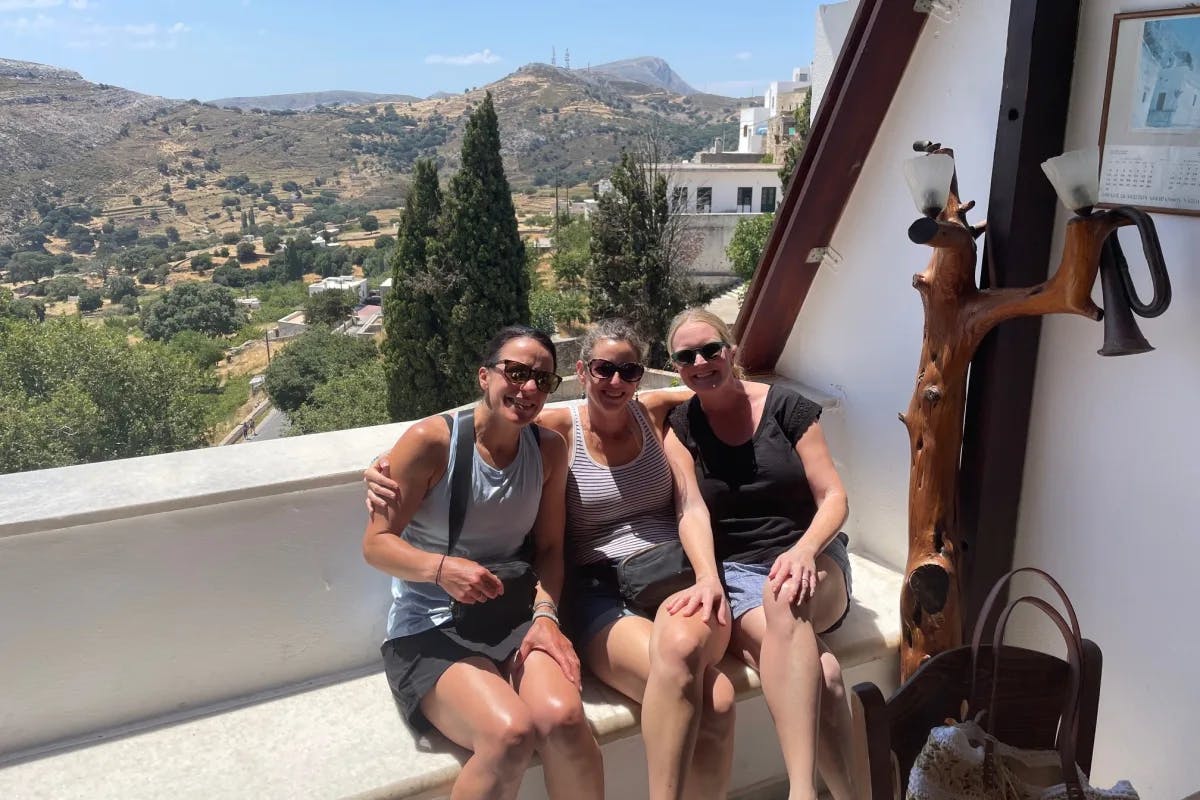 Three women on a bench on an outdoor patio overlooking a hillside.