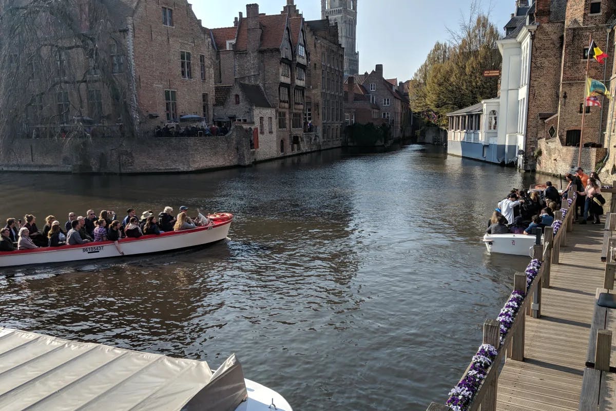 A boat full of people going down a river surrounded by stone buildings and trees. 