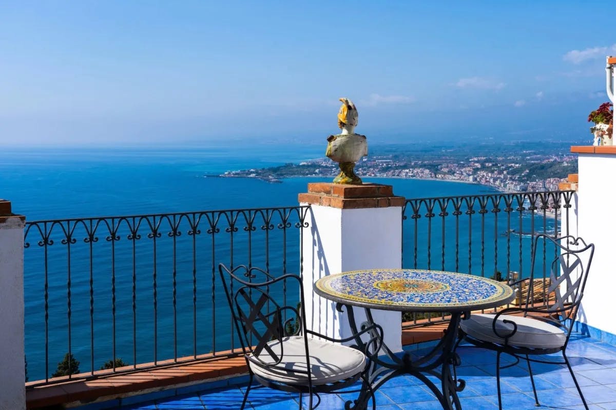 two chairs and a table on a blue tiled terrace high above the sea with amazing views of the coastline